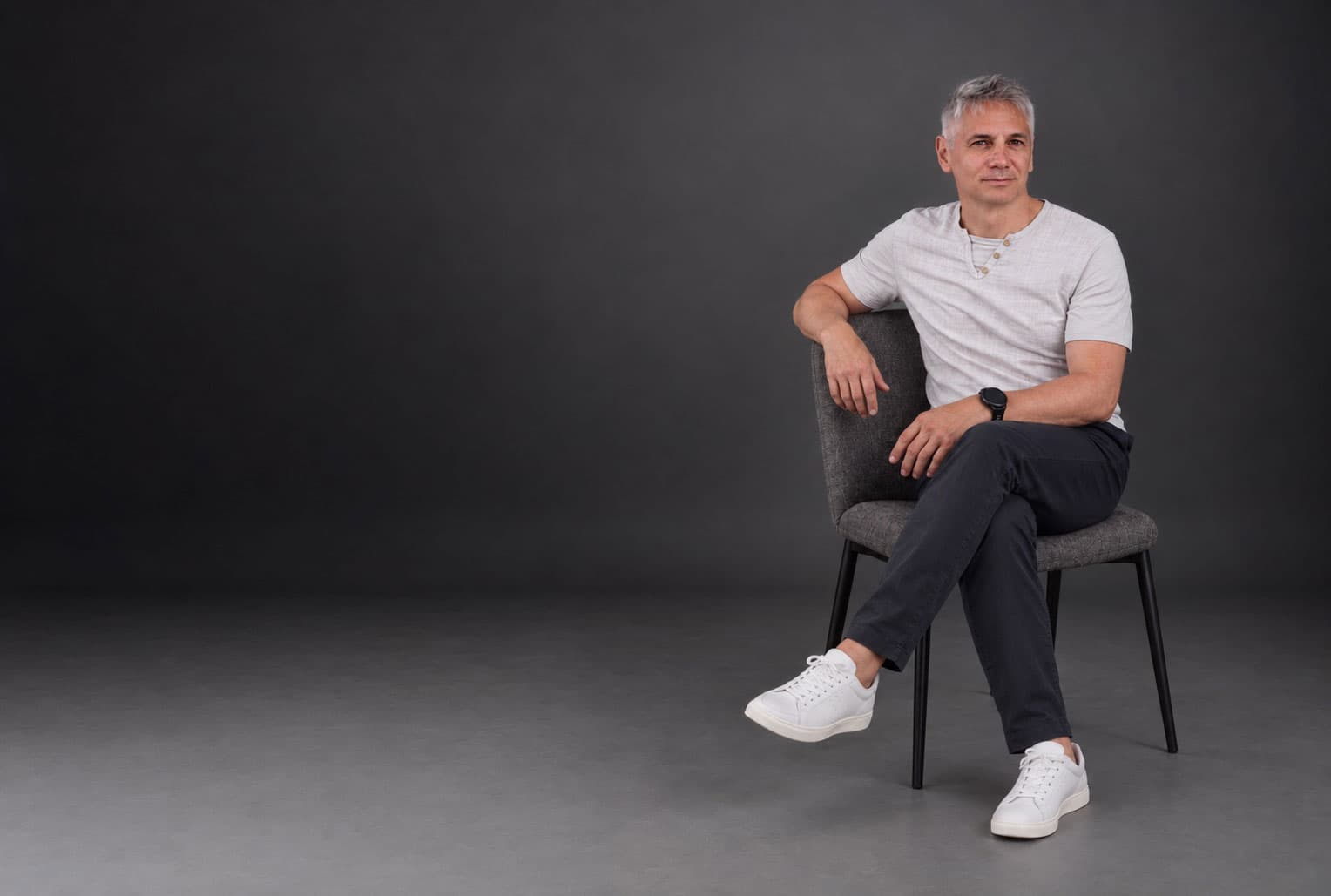 David Paci, Gründer und Inhaber von webse.at, sitzt auf einem Stuhl vor einer dunkelgrauen Wand. Foto, mit KI bearbeitet.